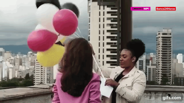#PRATODOSVEREM: Nath e Tainá estão no topo de um prédio. A Tainá está segurando a lista de preceitos presa a balões de festa e solta os balões no ar. Na sequência, a câmera acompanha os balões voando no céu.